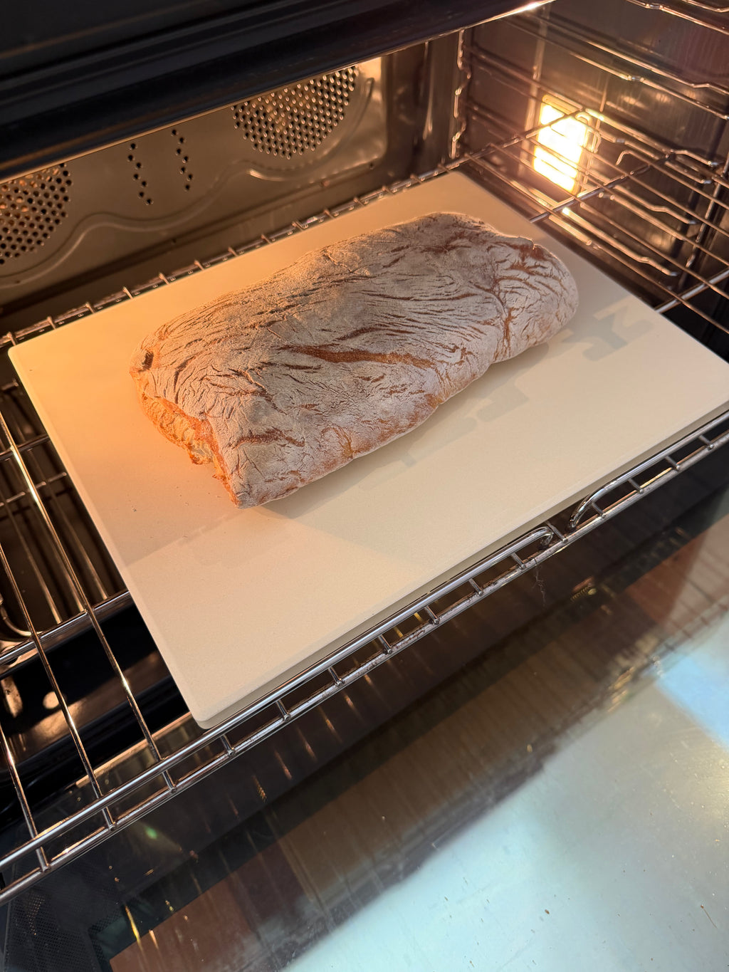 Loaf of bread baking inside an oven on a white sheet of paper.