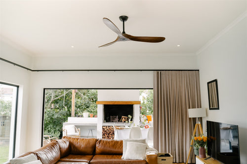 Modern living room with a brown leather sofa, ceiling fan, and large windows.