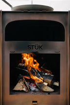Wood-burning stove with flames inside, branded 'STÜk'.