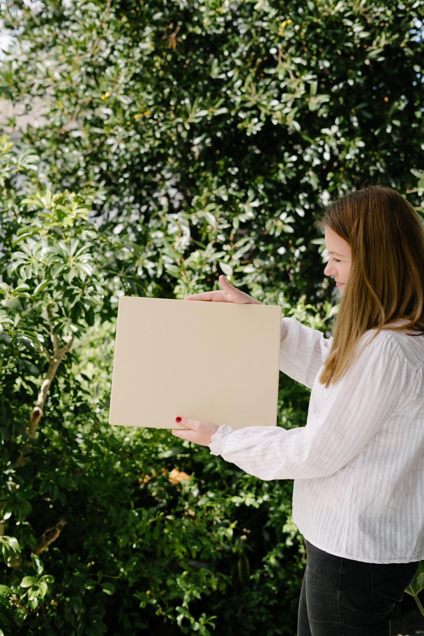 Woman holding a beige square in front of a green leafy background