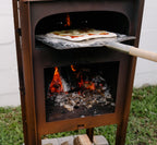 Wood-fired pizza oven with pizza being cooked and firewood on a brick base.