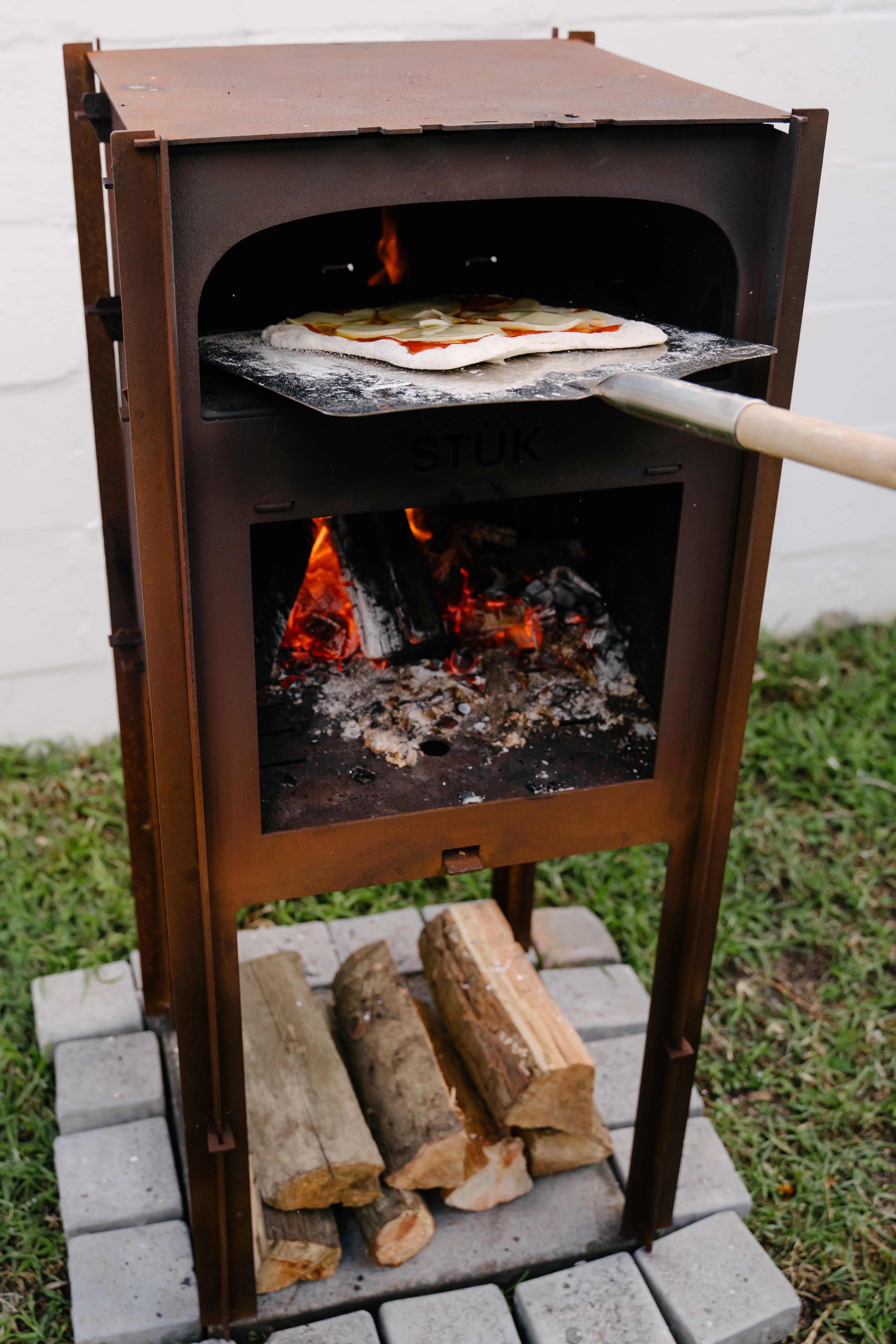 Wood-fired pizza oven with pizza being cooked and firewood on a brick base.