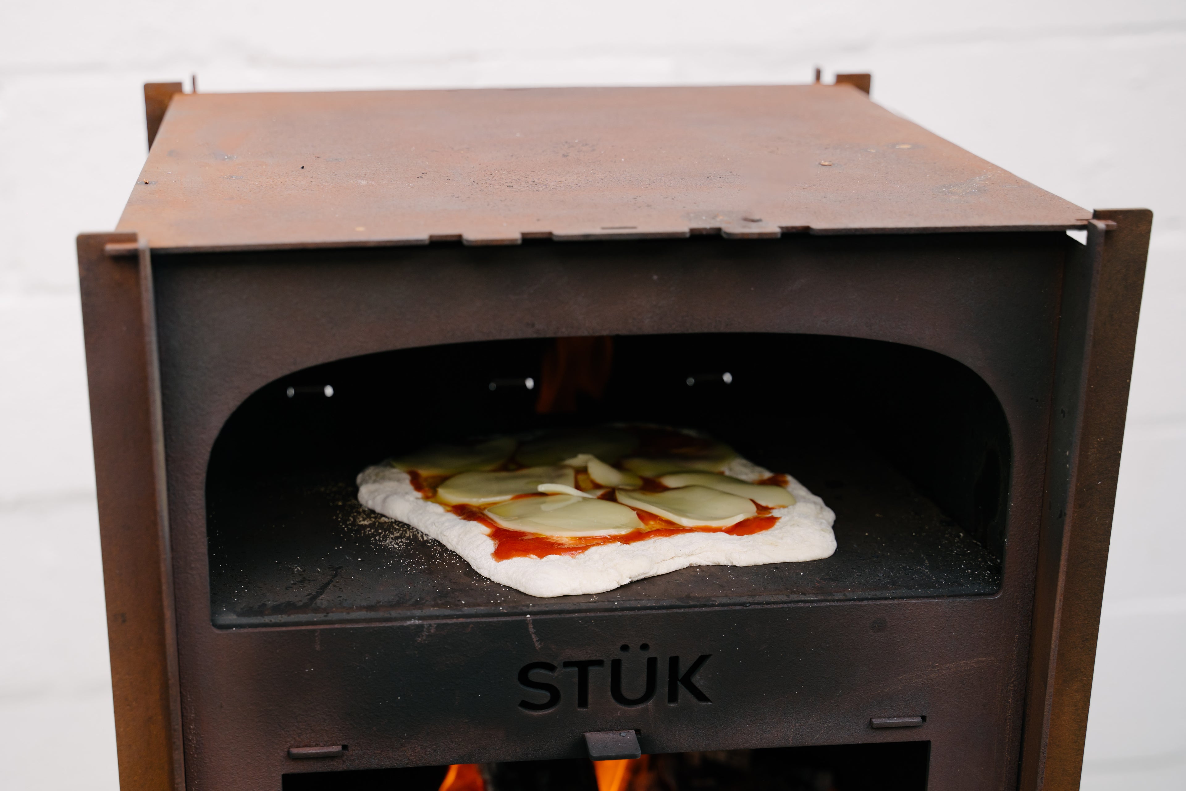 Wood-fired pizza oven with a pizza inside on a white background