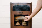 Person loading wood into a STÜk fireplace with smoke rising.