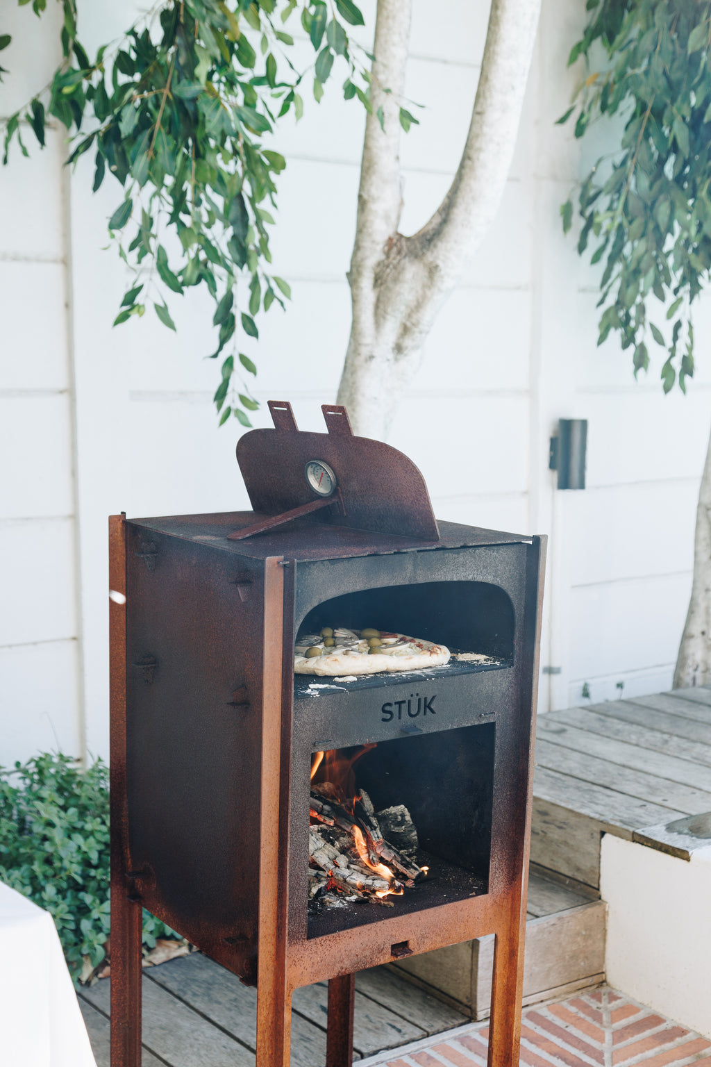 Outdoor pizza oven with 'STUK' branding on a wooden deck with plants in the background