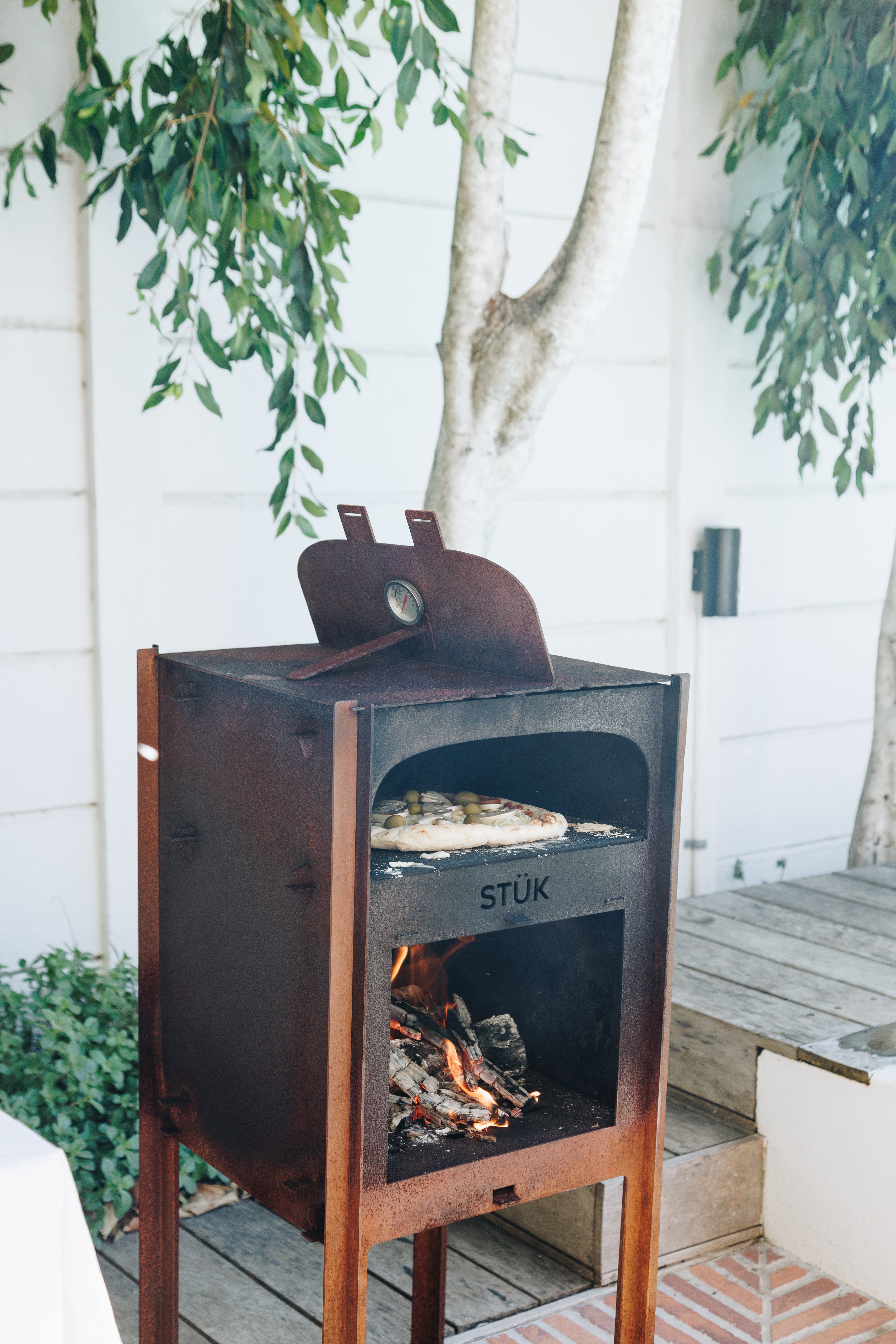 Outdoor pizza oven with 'STUK' branding on a wooden deck with plants in the background