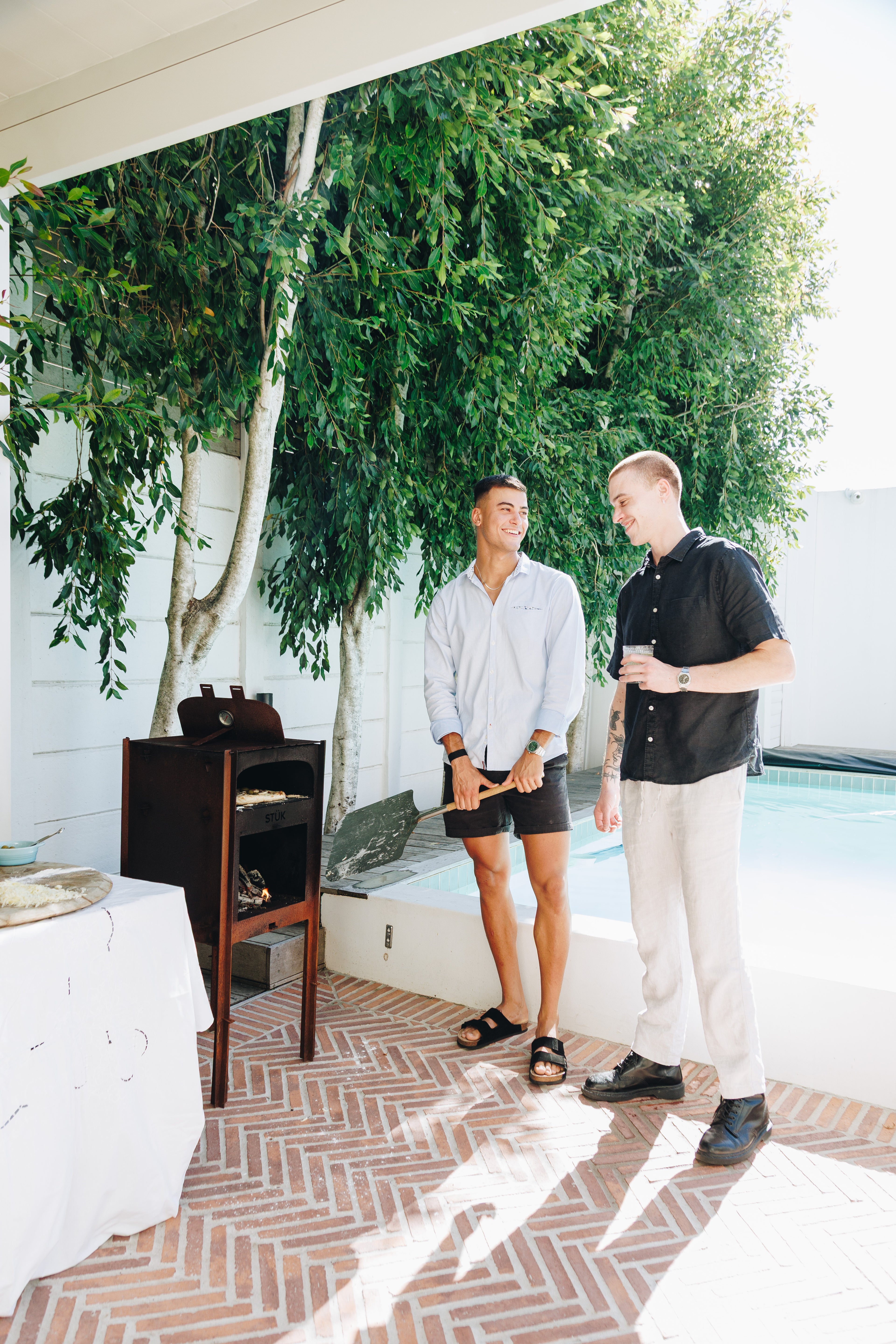 Two men standing by a poolside with greenery in the background