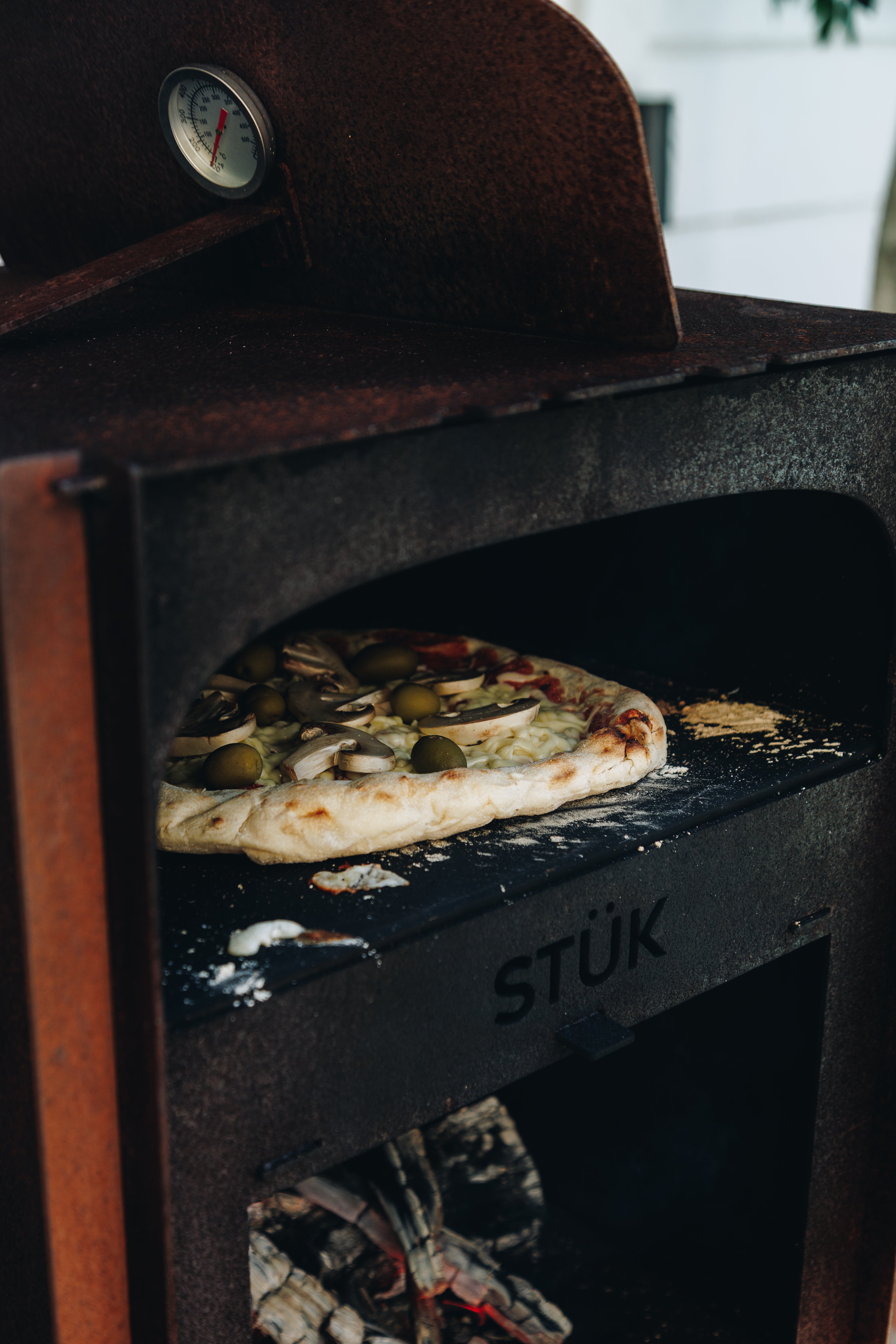 Pizza baking inside a 'STÜk' outdoor pizza oven with visible ingredients.