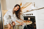 Woman placing a pizza into an oven in a kitchen