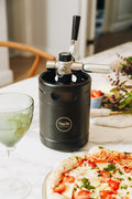 Black Taplit beer keg on a table with pizza and a glass of limeade.