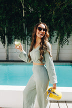 Woman in a light green outfit holding a glass by a poolside