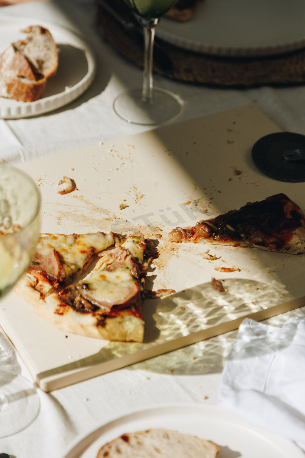 Pizza slices on a wooden board with a glass of wine and bread in the background