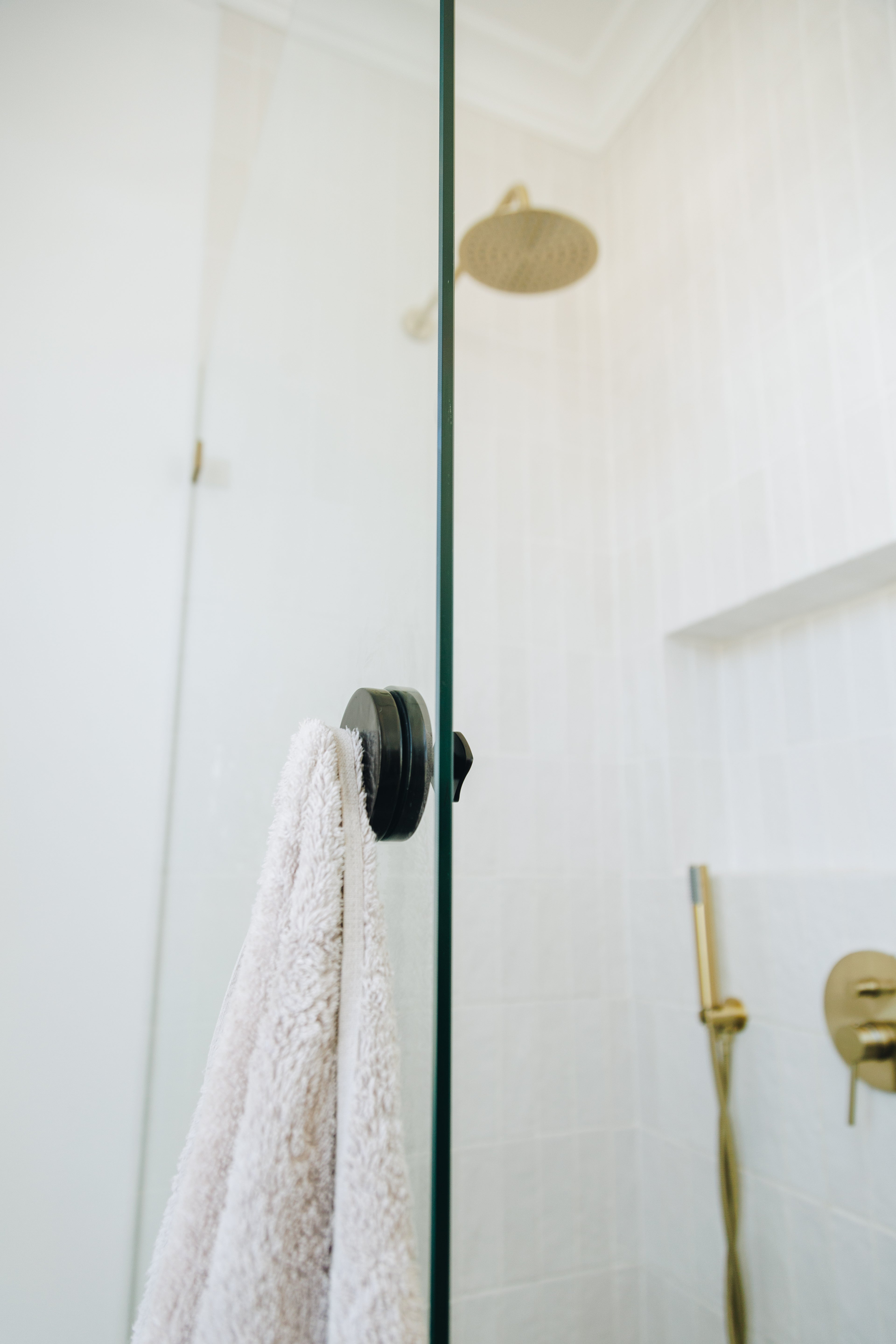 Shower with glass door, white towel, and gold fixtures in a bathroom setting.